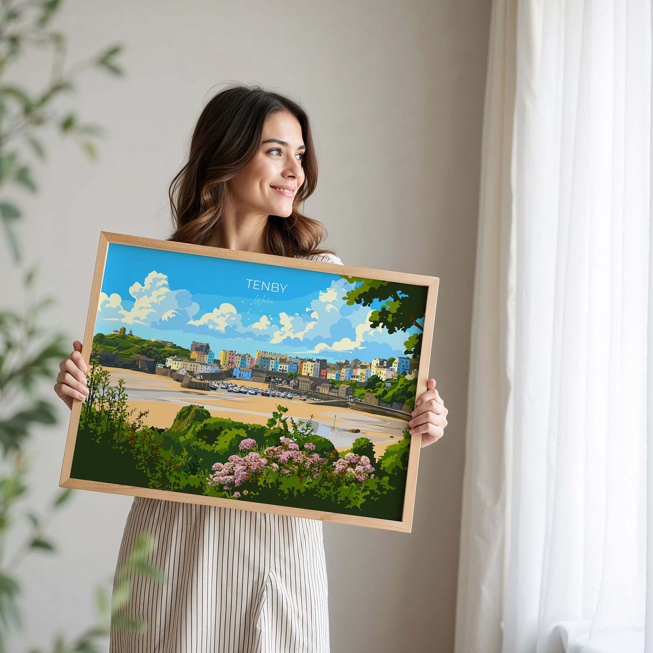 A woman is holding a framed picture of a coastal town, with a beach, buildings, and flowers visible in the image.