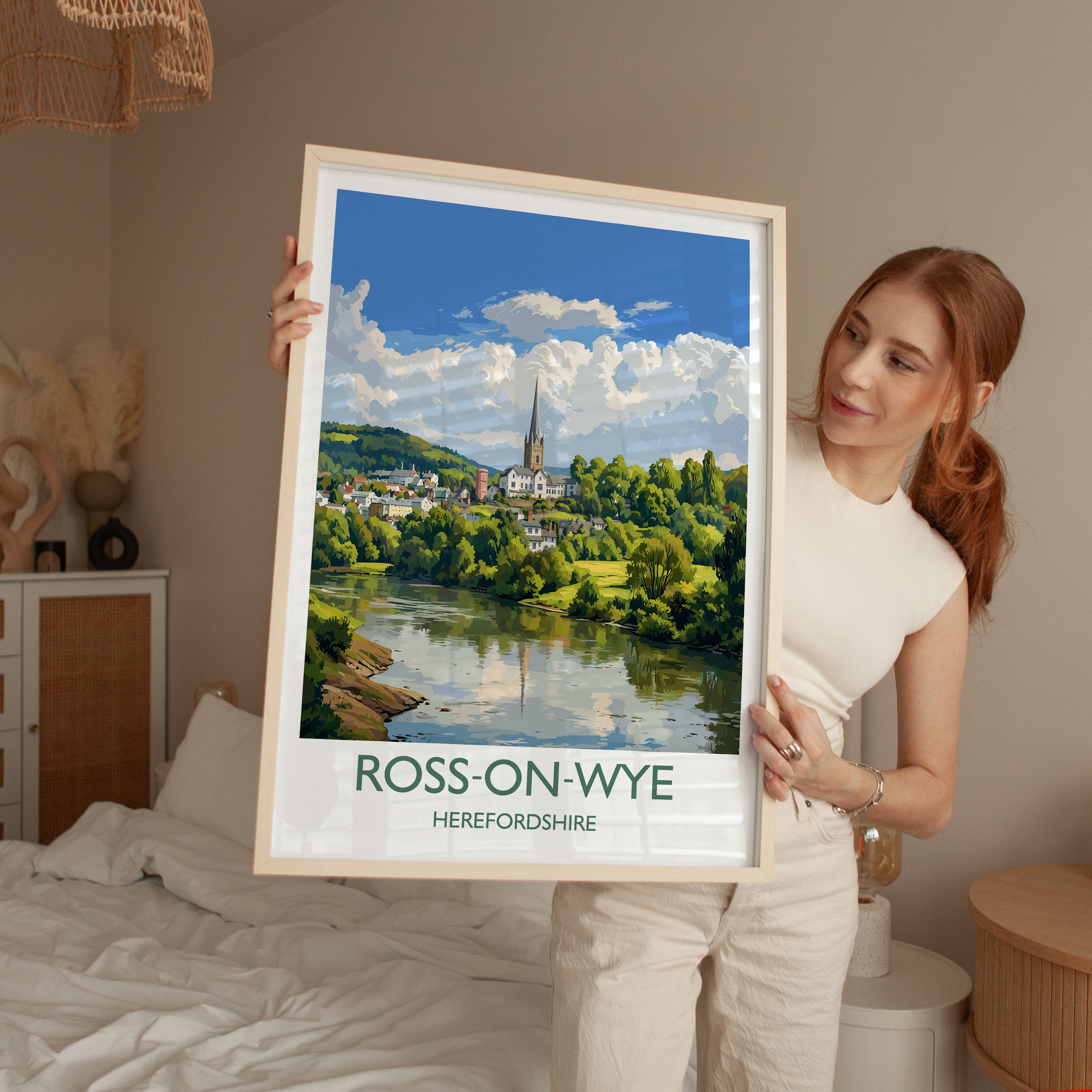 A woman holds up a framed poster of Ross-on-Wye, a town in Herefordshire, England, with a scenic view of the town and its surroundings.