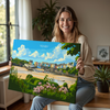 A woman is sitting on a wooden bench and holding up a large canvas print of a scenic coastal town.