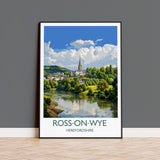The image is a framed poster depicting a scenic view of Ross-on-Wye, a town in Herefordshire, England. The poster showcases a picturesque landscape with a river, lush greenery, and a church spire in the distance. The text "ROSS-ON-WYE" and "HEREFORDSHIRE" is prominently displayed, indicating the location of the scene.