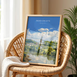 a framed painting of a scenic landscape with a church spire, a river, and a town in the background.
