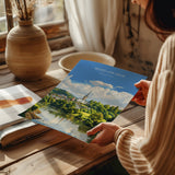 A person is holding a printed calendar featuring a scenic landscape with a river and a church spire.
