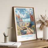 A framed poster of a coastal village in Kent, England, featuring a boat on the shore and colorful houses along the beach.